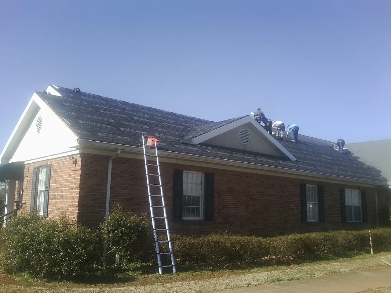 Crew tearing shingles off a brick ranch roof with a ladder set — Emergency Roof Repair work by our crew in Kingstree