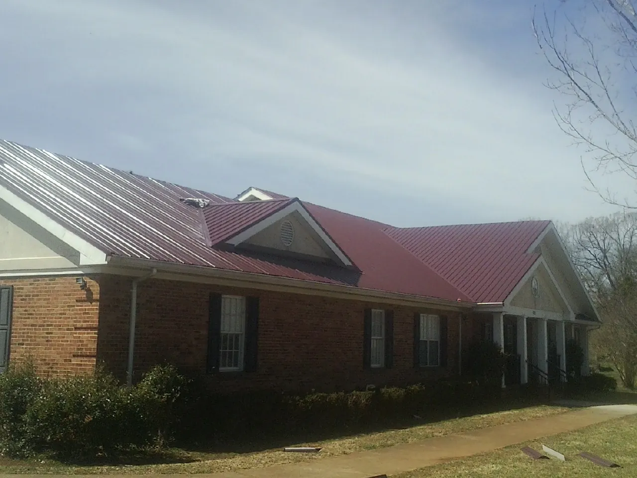 Red metal roof with gabled entries on a long brick building, from a Hail Damage Roof Repair job in Kingstree