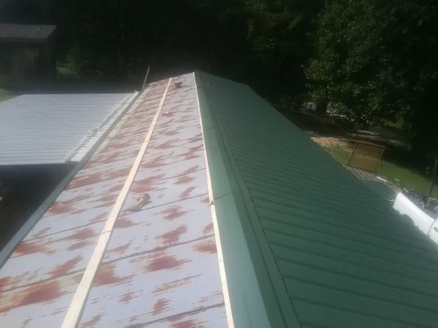 Old rusted panels beside newly installed green metal roofing — Wind Damage Roof Repair by Roofing Brothers in Kingstree