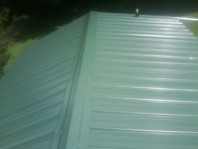 New green metal panels meeting at the ridge of a roof — Flat Roof Repair work by our crew in Kingstree