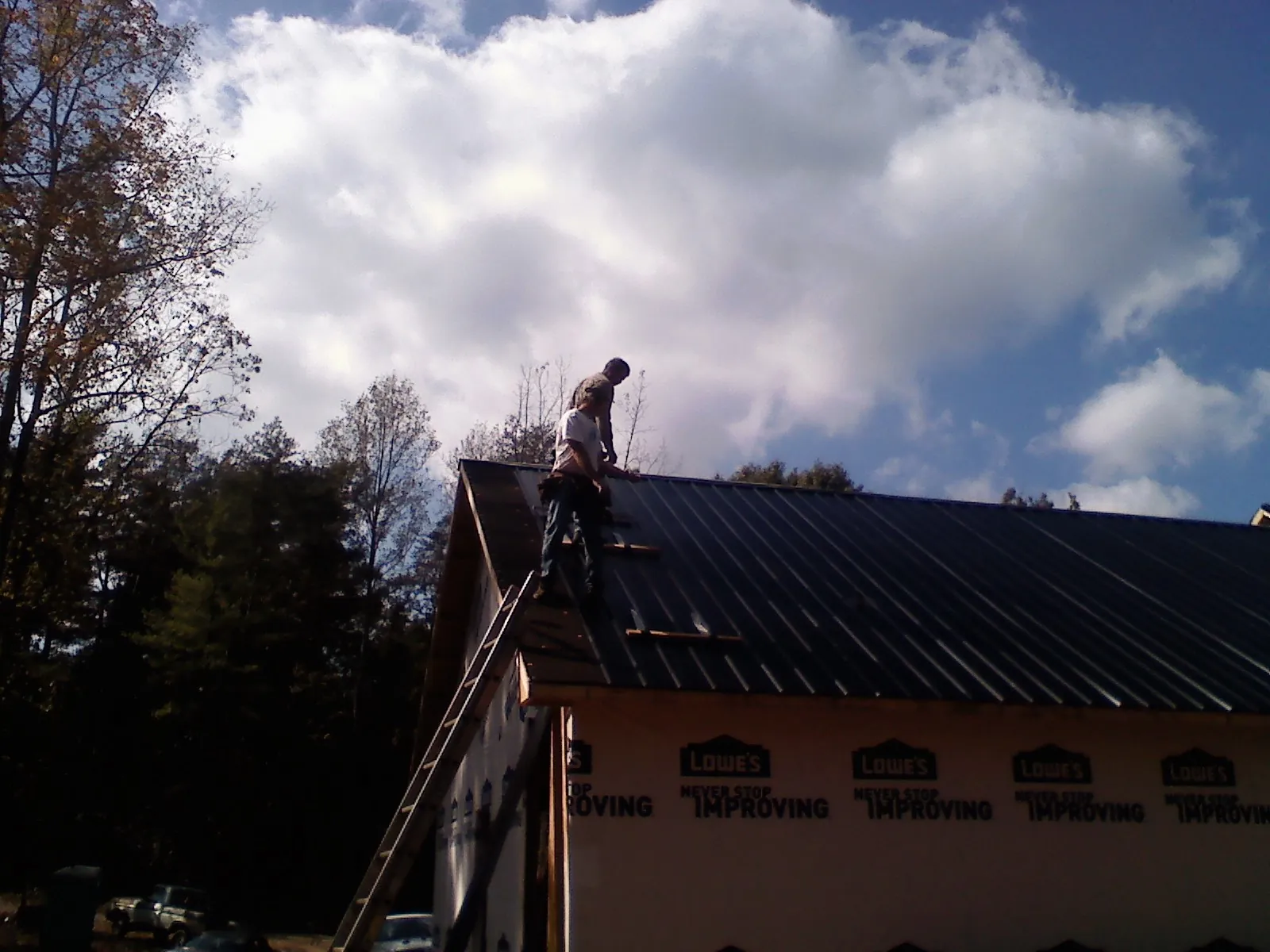 Roofer fastening dark metal panels high against a cloudy sky, from a Roof Inspection job in Kingstree